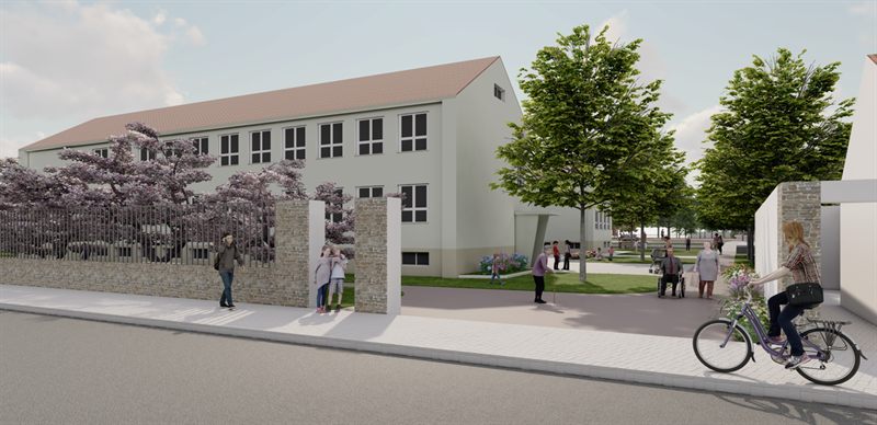 The main entrance from the street: a stone-faced boundary wall with railings and a flowering cherry behind it, the three-storey former school building with a pitched tiled roof, and the pink dyed-concrete activity lane running in through the gate, with a child, an older woman with a walking stick, a man in a wheelchair and a cyclist arriving.