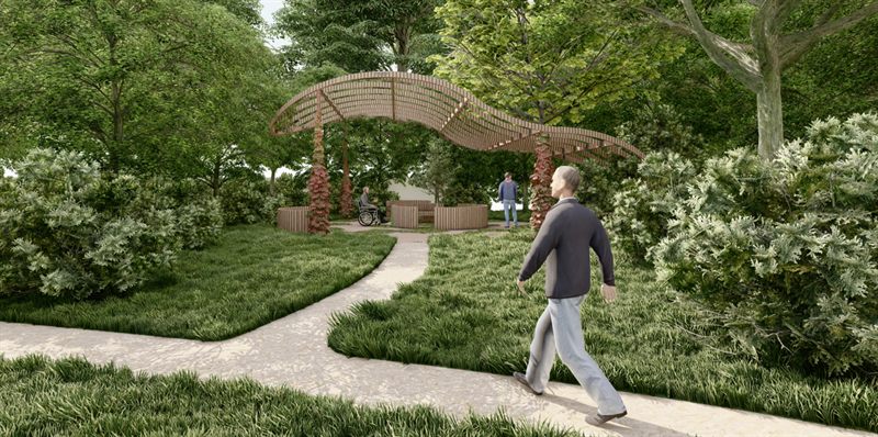 The quiet zone pavilion: an undulating timber slatted canopy on posts climbed by red ivy, over a ring of curved timber seating where a man in a wheelchair sits, reached by a pale trail through long grass and dense shrubs under mature trees, with an older man walking along the trail in the foreground.